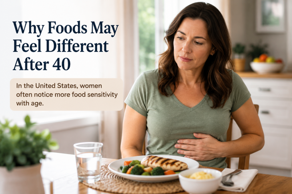 American woman in her 40s sitting at a dining table after a healthy meal, gently holding her stomach and reflecting on how food affects digestion as she ages.